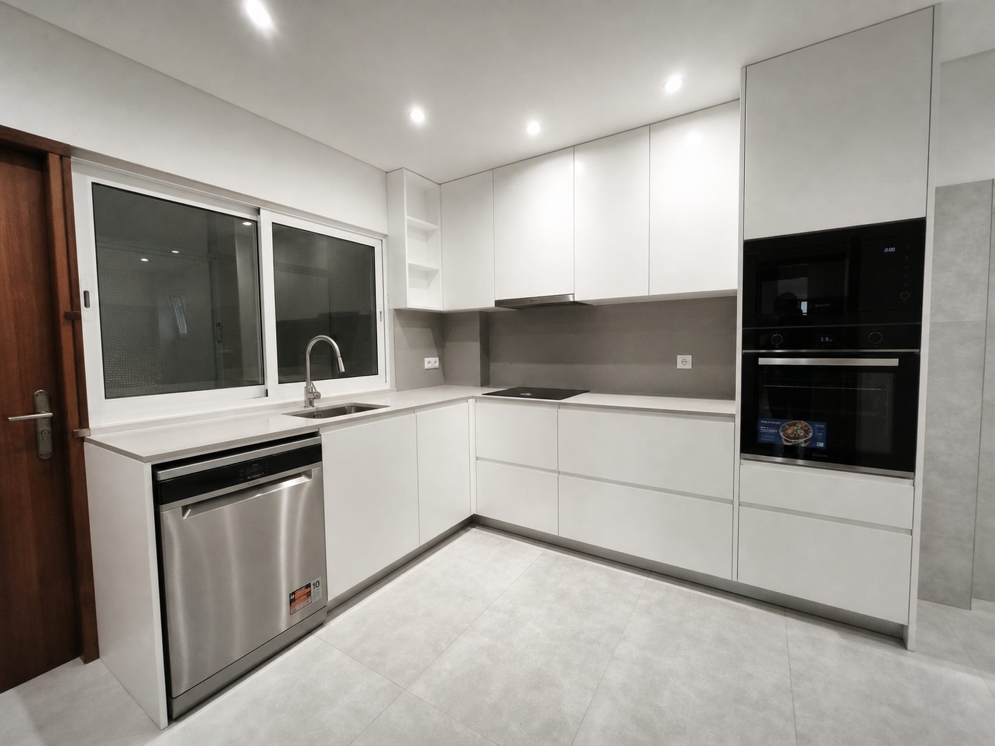 Cozinha branca renovada com caixilharia branca, iluminação embutida e bancada funcional